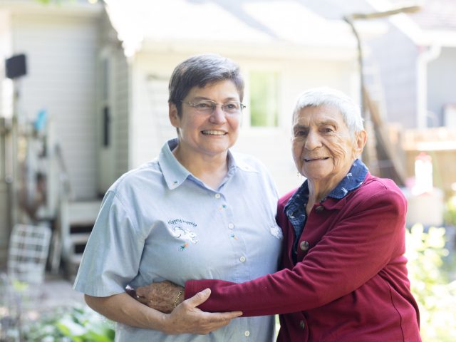 Two direct care workers standing at the center of the picture and hugging.