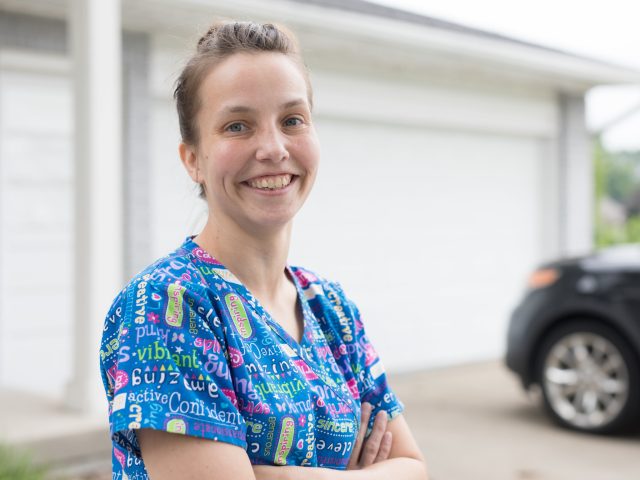 Direct care worker, wearing scrubs, looking at the camera and smiling.