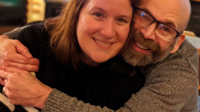 Dan and Jen, a married couple hugging each other and smiling to the camera.