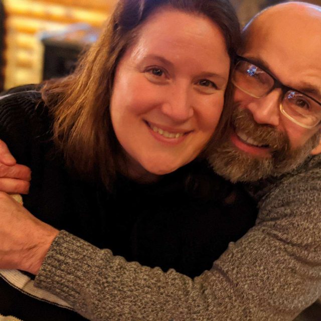 Dan and Jen, a married couple hugging each other and smiling to the camera.