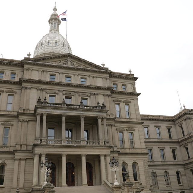Exterior view of the Michigan State Capitol building on an overcast day, showing its domed roof, grand staircase, and historic stone architecture.