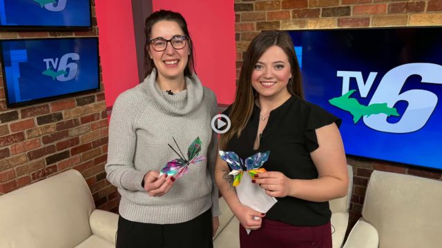Two women hold paper butterflies for a report on TV6 news.