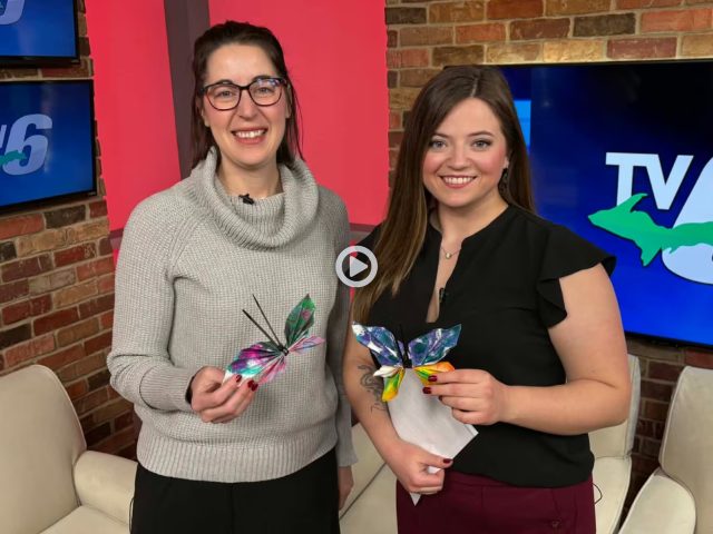 Two women hold paper butterflies for a report on TV6 news.
